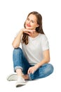 Young cherful woman in jeans, white t-shirt, sneakers sits on the floor and smiles. isolated on white background