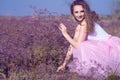 Young chic woman with long waving hair and artistic make up sitting on the field of violet flowers looking aside and smiling. Royalty Free Stock Photo