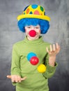 Young child dressed as a clown with wig and fake nose has fun playing with colorful balls celebrating carnival Royalty Free Stock Photo