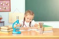 Young child girl drawing or writing with colorful pencils in notebook in school over blackboard Royalty Free Stock Photo