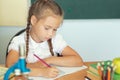 Young child girl drawing or writing with colorful pencils in notebook in school over blackboard Royalty Free Stock Photo