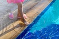 Young child girl in pink dress and shoes standing barefoot at the edge of a swimming pool try with her leg cool blue water, Royalty Free Stock Photo