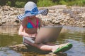 Young child girl sitting on stone in river water with laptop Summer vacation and holiday concept, studying online with tablet, Royalty Free Stock Photo