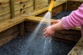 Young child holds hands under water hose spray at vegetable box in garden. Royalty Free Stock Photo