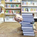 Child peeking behind a stack of books at the library