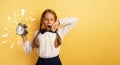 Young child student with ringing alarm clock is lazy going to school. Yellow background