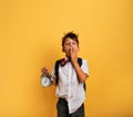 Young child student with ringing alarm clock is lazy going to school. Yellow background.