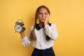 Young child student with ringing alarm clock is lazy going to school. Yellow background