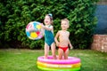 Young children siblings play large inflatable beach ball in courtyard of house in swimming pool. theme of heat and water games,