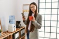 Young chinese businesswoman using smartphone and drinking coffee at the office Royalty Free Stock Photo