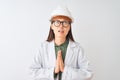 Young chinese engineer woman wearing coat helmet glasses over isolated white background begging and praying with hands together Royalty Free Stock Photo