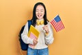 Young chinese girl exchange student holding america flag sticking tongue out happy with funny expression