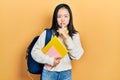 Young chinese girl holding student backpack and books asking to be quiet with finger on lips