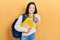 Young chinese girl holding student backpack and books pointing to you and the camera with fingers, smiling positive and cheerful Royalty Free Stock Photo