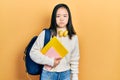 Young chinese girl holding student backpack and books puffing cheeks with funny face
