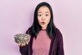 Young chinese girl holding sunflower seeds bowl scared and amazed with open mouth for surprise, disbelief face Royalty Free Stock Photo