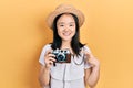 Young chinese girl wearing summer hat holding vintage camera smiling happy pointing with hand and finger Royalty Free Stock Photo