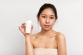 Young chinese lady wrapped in towel showing deodorant, posing after shower on white studio background Royalty Free Stock Photo