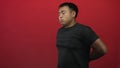 Young chinese man in black t shirt grimacing holds lower back with backache in red studio; perseverance Royalty Free Stock Photo