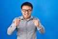 Young chinese man standing over blue background excited for success with arms raised and eyes closed celebrating victory smiling Royalty Free Stock Photo