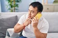 Young chinese man talking on the smartphone with doubt expression at home Royalty Free Stock Photo