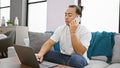 Young chinese man using laptop talking on smartphone sitting on sofa at home Royalty Free Stock Photo