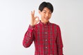 Young chinese man wearing casual red shirt standing over isolated white background smiling positive doing ok sign with hand and Royalty Free Stock Photo