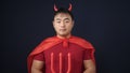 Young chinese man wearing devil costume holding trident over isolated black background