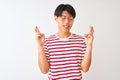 Young chinese man wearing glasses and striped t-shirt standing over isolated white background gesturing finger crossed smiling Royalty Free Stock Photo