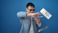 Young chinese man wearing thug life glasses throwing dollars over isolated blue background