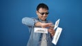 Young chinese man wearing thug life glasses throwing dollars over isolated blue background