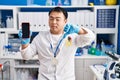 Young chinese man working at scientist laboratory holding smartphone with angry face, negative sign showing dislike with thumbs Royalty Free Stock Photo