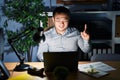 Young chinese man working using computer laptop at night with a big smile on face, pointing with hand and finger to the side Royalty Free Stock Photo