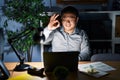 Young chinese man working using computer laptop at night smiling positive doing ok sign with hand and fingers Royalty Free Stock Photo