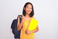 Young chinese student woman wearing backpack holding book over isolated white background pointing and showing with thumb up to the Royalty Free Stock Photo