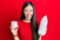 Young chinese woman drinking a glass of fresh milk sticking tongue out happy with funny expression