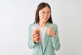 Young chinese woman drinking tomato smoothie over isolated white background happy with big smile doing ok sign, thumb up with Royalty Free Stock Photo