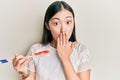 Young chinese woman eating prawn sushi using chopsticks covering mouth with hand, shocked and afraid for mistake