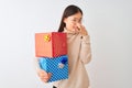 Young chinese woman holding birthday gifts over isolated white background smelling something stinky and disgusting, intolerable