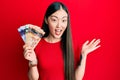 Young chinese woman holding canadian dollars celebrating achievement with happy smile and winner expression with raised hand