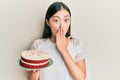 Young chinese woman holding carrot cake covering mouth with hand, shocked and afraid for mistake Royalty Free Stock Photo