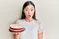 Young chinese woman holding carrot cake scared and amazed with open mouth for surprise, disbelief face Royalty Free Stock Photo