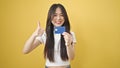 Young chinese woman pointing to credit card doing ok gestur over isolated yellow background