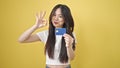 Young chinese woman pointing to credit card doing ok gestur over isolated yellow background