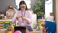 Young chinese woman preschool teacher pealing banana sitting on table at kindergarten