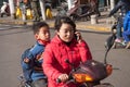 Young chinese woman riding a scooter talking in mobile cell phone with a child on the back seat