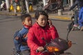 Young chinese woman riding a scooter talking in mobile cell phone with a child on the back seat. Beijing