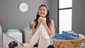 Young chinese woman smelling clean towel standing by clothesline smiling at laundry room
