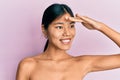 Young chinese woman standing topless showing skin very happy and smiling looking far away with hand over head Royalty Free Stock Photo