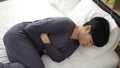 Young chinese woman suffering for menstrual pain lying on bed at bedroom Royalty Free Stock Photo